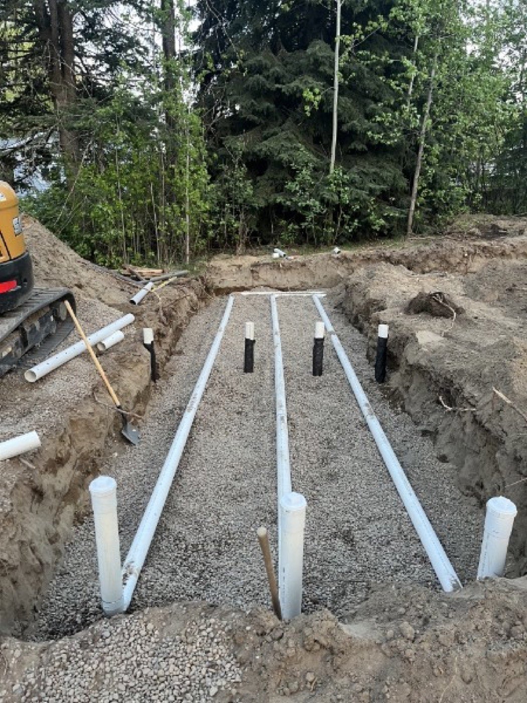 Distribution piping laid in a gravel bed, with part of the excavator visible beside the work