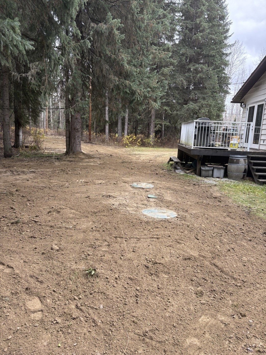 Regraded ground around septic access lids beside an existing home